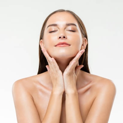 skin_flooding Frau mit strahlender Haut, die ihre Wangen sanft berührt, symbolisiert die Skin Flooding Methode für intensive Hydratation in der Hautpflege.