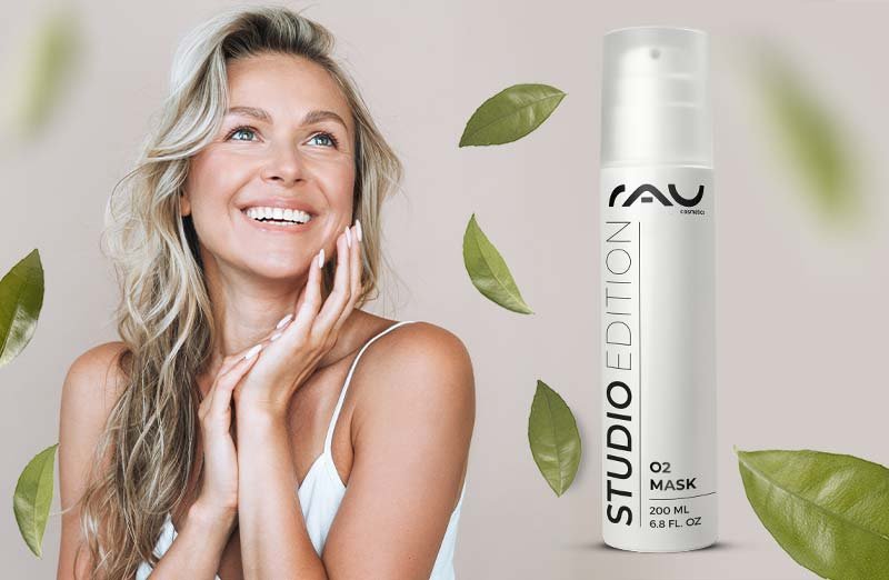 Frau mit strahlendem Lächeln und jugendlicher Haut, präsentiert die RAU O2 Mask in einem hygienischen Airless-Spender, umgeben von grünen Blättern, symbolisiert Frische und Hautpflege.