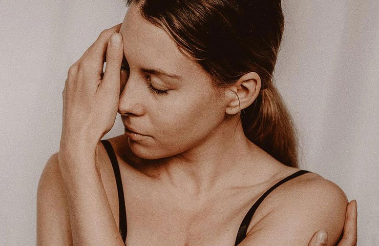 Frau mit geschlossenen Augen und Hand an der Stirn, symbolisiert Entspannung und Lymphdrainage zur Bekämpfung von Wassereinlagerungen im Gesicht.