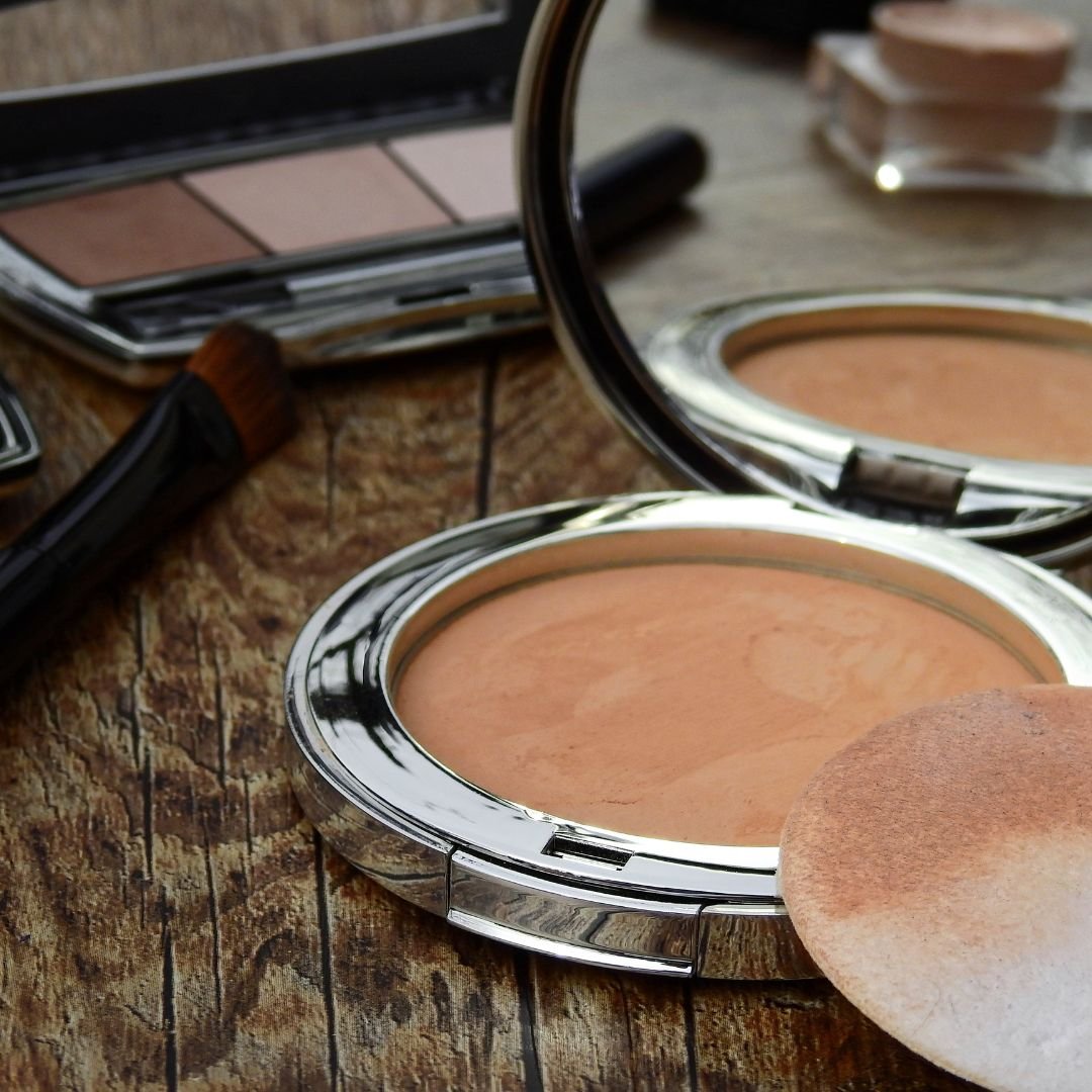 Make-up-Kompaktdose mit Puder, Pinsel und weiteren Kosmetika auf einer Holzoberfläche, die Schönheitsprodukte für Hautpflege und Make-up zeigt.