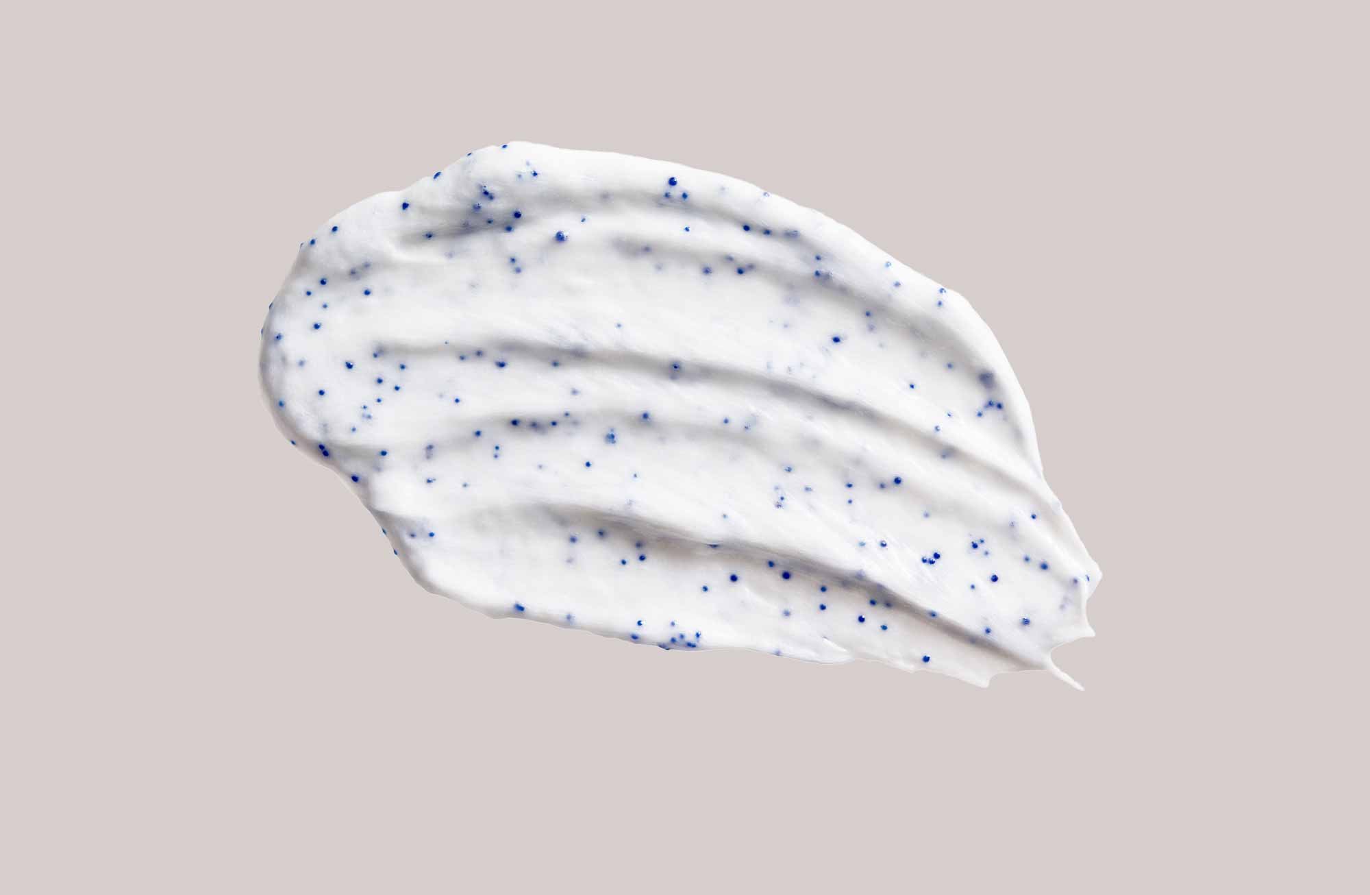 RAU Cosmetics Gesichts- und Körperpeeling: cremige weiße Textur mit blauen Sprenkeln auf hellem beige Hintergrund.