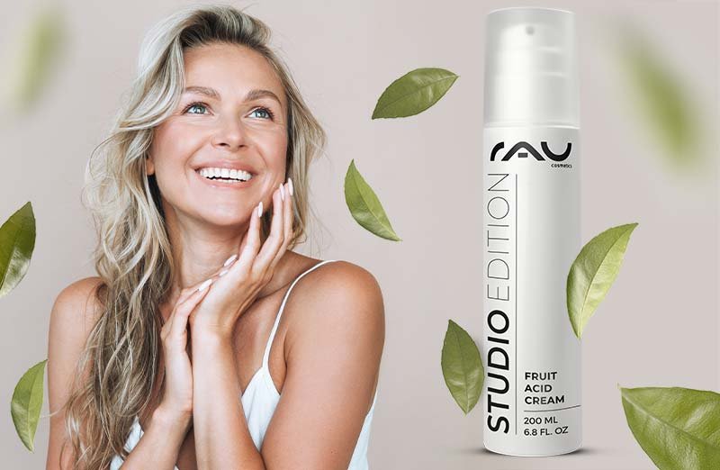 Lächelnde Frau mit RAY Fruchtsäurecreme, umgeben von grünen Blättern, zeigt das Produkt und seine Funktionen.