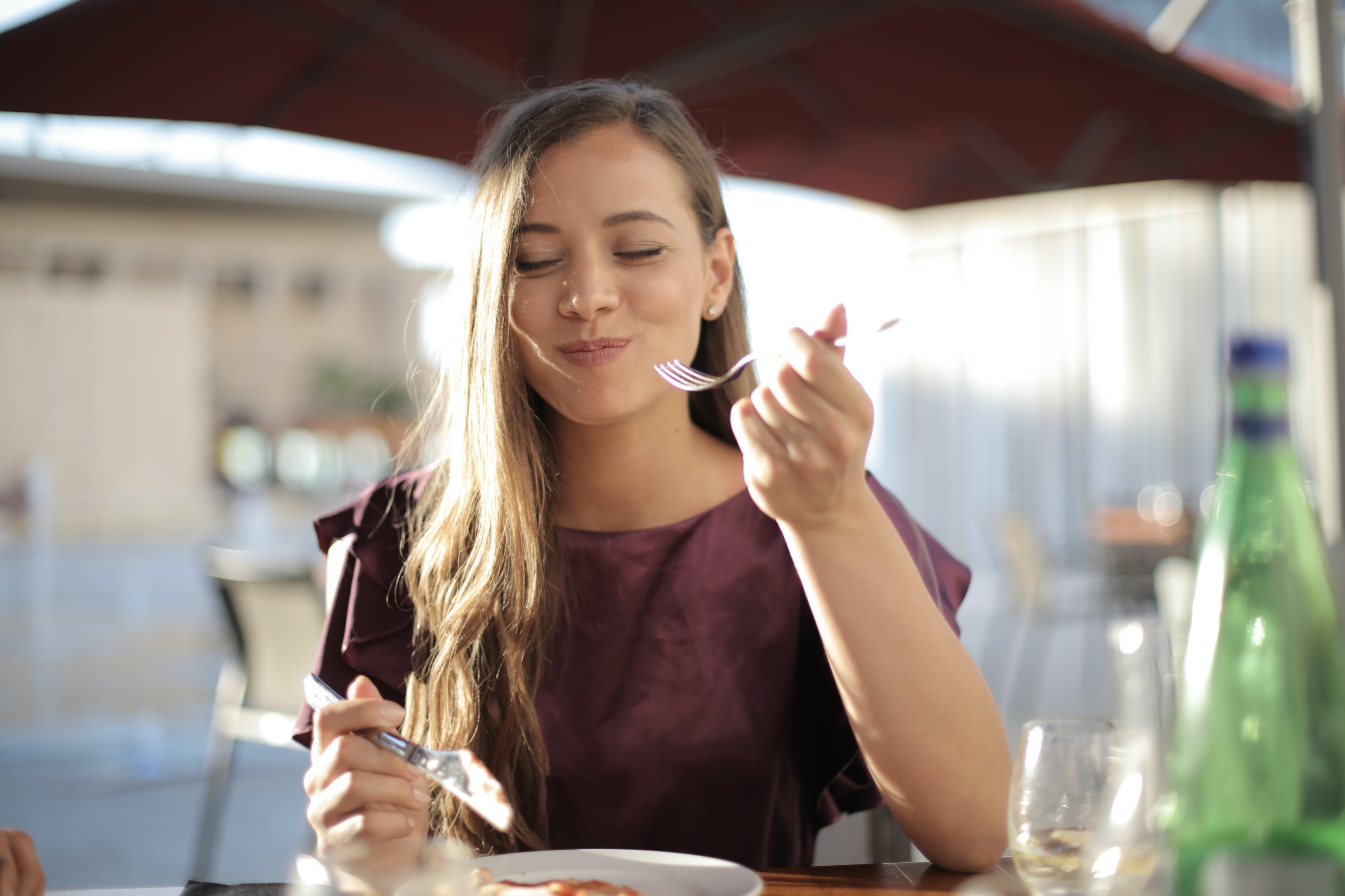 Frau genießt Essen in einem Restaurant, lächelt und hält eine Gabel, symbolisiert den Zusammenhang zwischen Ernährung und Hautgesundheit.