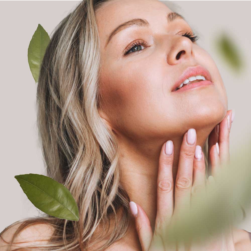 RAU_Cosmetics-wirkstoffkosmetik-gesichtspflege-hautpflege-onlineshop-kosmetik-kosmetikstudio-kabinenware-passion Frau mit blonden Haaren, die sanft ihren Hals berührt, umgeben von grünen Blättern, symbolisiert hochwertige Hautpflege und natürliche Inhaltsstoffe von RAU Cosmetics.