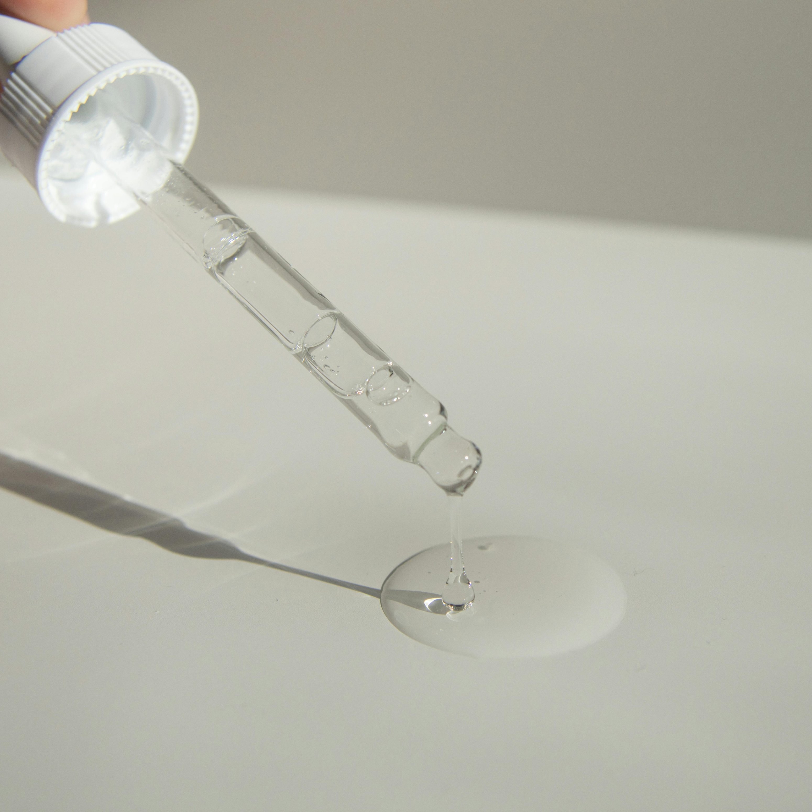 Eine Pipette gibt klares Serum auf eine Oberfläche ab und hebt die Anwendung von Hautpflegeprodukten im Zusammenhang mit Peptiden und Anti-Aging-Vorteilen hervor.