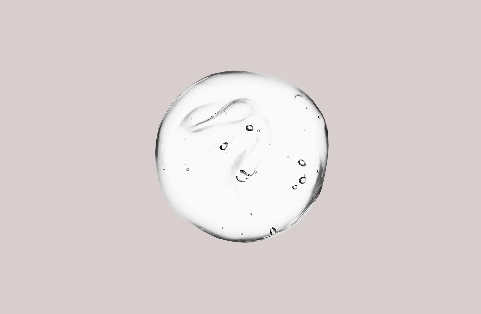 Transparente Gel-Substanz mit Luftblasen auf neutralem Beigehintergrund, passend zu RAU Cosmetics Anti-Rötungsserum.