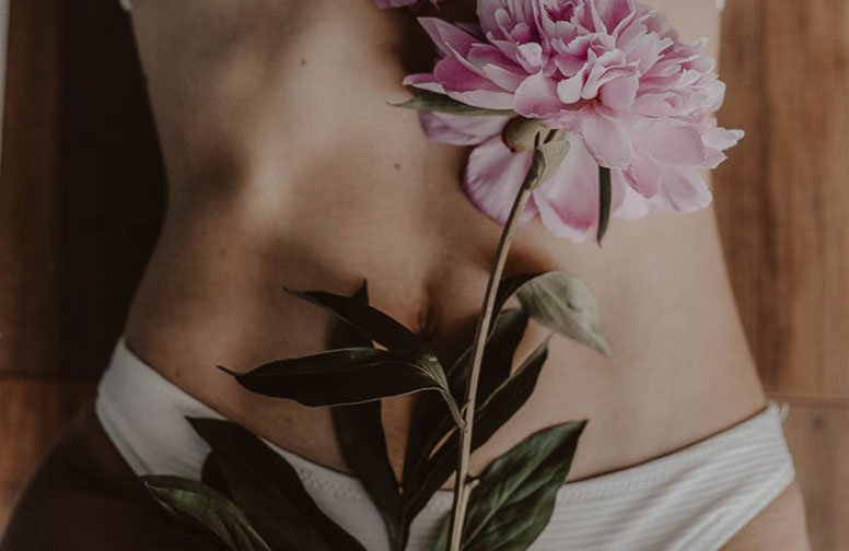 Frau mit Blumenarrangement auf dem Bauch, symbolisiert Hautpflege und Wohlbefinden im Kontext von Darmgesundheit und Enterotypen.