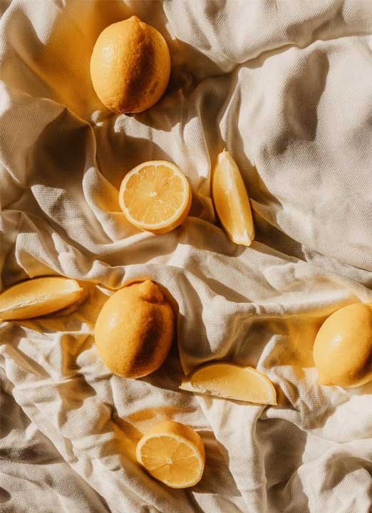 Frische Zitronen und Zitronenscheiben auf einem weißen Stoff, symbolisierend die Verwendung von Fruchtsäuren in der Hautpflege.
